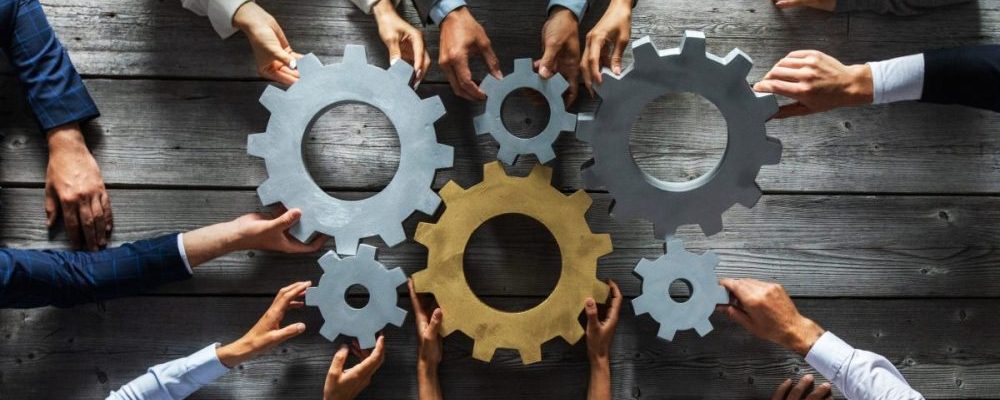Group of business people joining together silver and golden colored gears on table at workplace top view